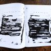A zine lays open on a wooden table. The pages show e-mails redacted with thick black markings. The remaining text reads as an experimental poem.