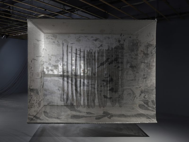 A transparent woven "prison cell" with black silk fabric suspended inside.